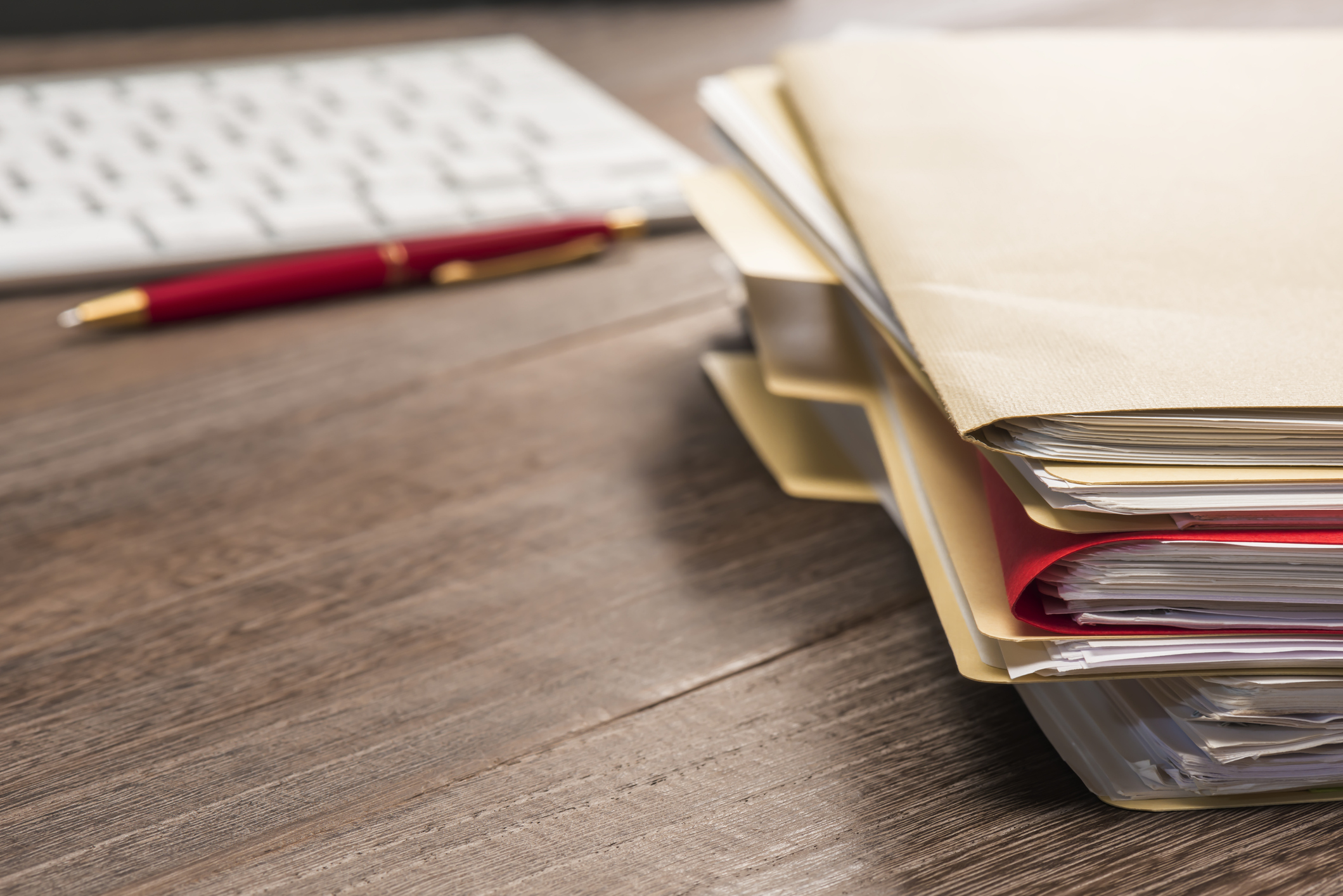 Stack of folders, pen and keyboard on a desk