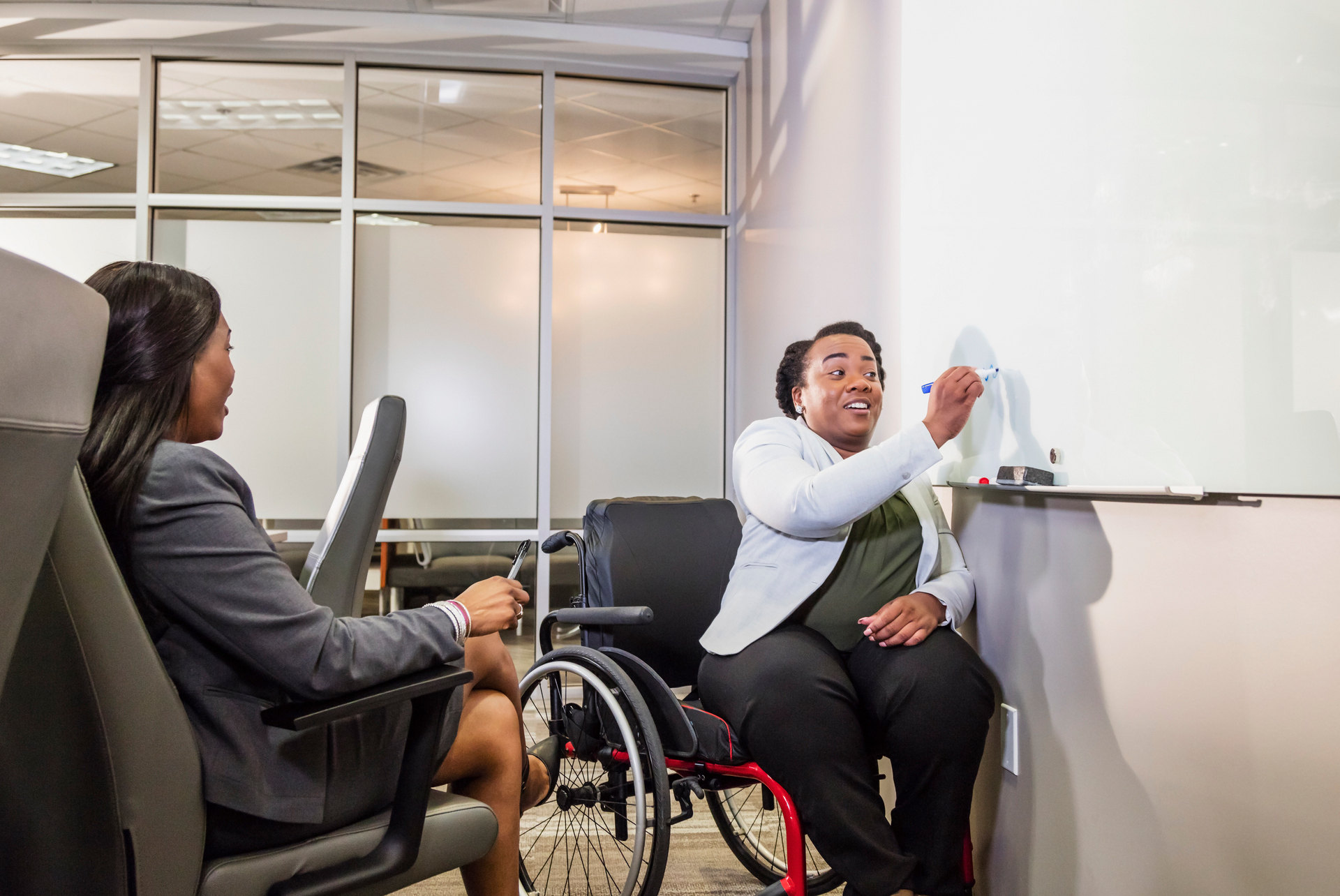 Coworkers in meeting room, one in wheelchair at whiteboard drawing